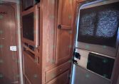 RV interior kitchen with tall wood cabinets, built-in microwave, and a stainless fridge beside a curved doorway