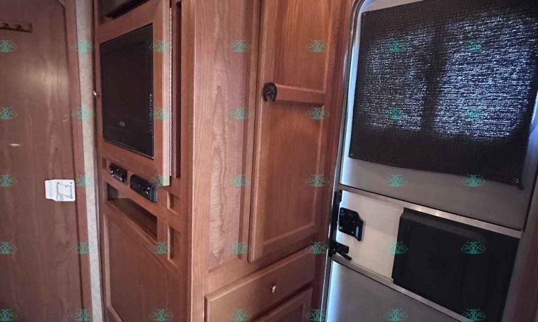 RV interior kitchen with tall wood cabinets, built-in microwave, and a stainless fridge beside a curved doorway