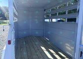 Interior of an empty aluminum trailer with a wooden floor and metal side rails, open rear ramp, outdoors on a sunny day