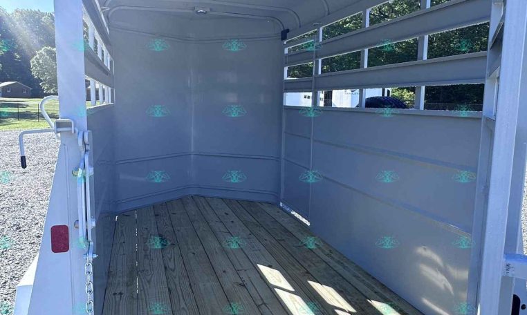 Interior of an empty aluminum trailer with a wooden floor and metal side rails, open rear ramp, outdoors on a sunny day