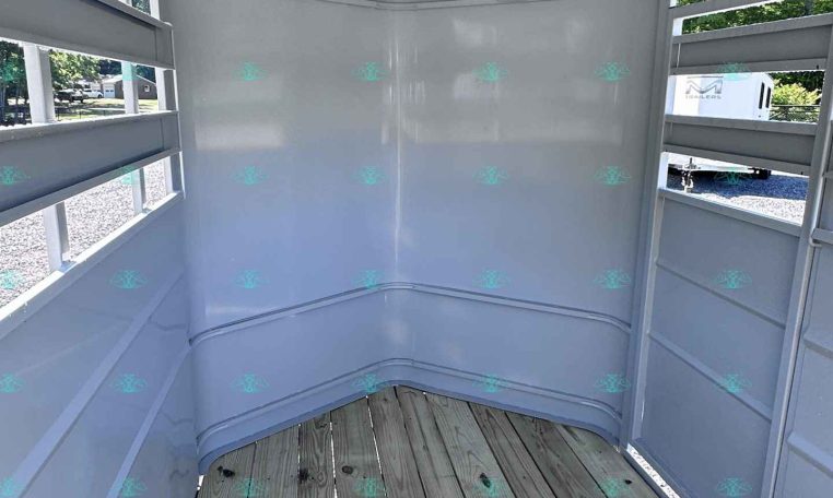 Interior of a white horse trailer with a wooden floor and open side doors, showing horizontal slatted windows and light from outside