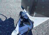 Close-up of a trailer hitch and jack on a white utility trailer, with a diamond-plate fender and propane tank, on gravel ground.