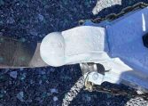 Close-up of a trailer hitch coupler with safety chains on a rocky gravel surface.