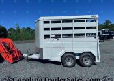 White Valley Trailers livestock trailer parked on a gravel lot with a red equipment attachment in the foreground and trees in the background