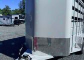 White livestock trailer with curved front and diamond-plate lower panel on a gravel lot