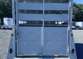 Rear of a white livestock trailer with double split doors, vented side panels, on a gravel lot with other trailers in the background