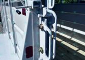 Close-up of a metal trailer latch and hasp securing a gate, with a safety chain visible on a gray trailer frame.
