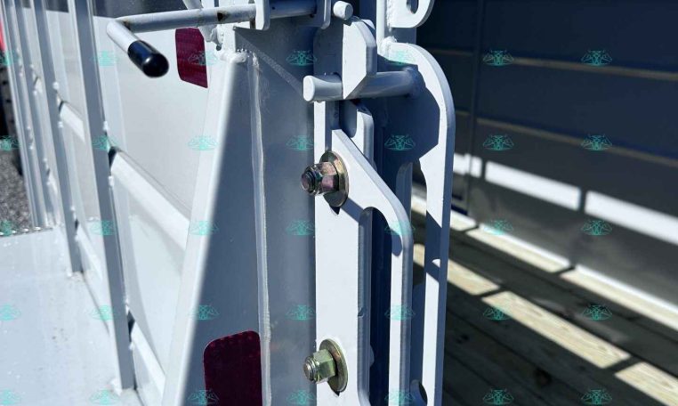 Close-up of a metal trailer latch and hasp securing a gate, with a safety chain visible on a gray trailer frame.