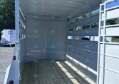 Open livestock trailer interior with wooden floor and white metal sides, ready for loading on a sunny day.”