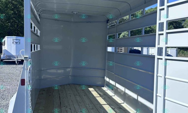 Open livestock trailer interior with wooden floor and white metal sides, ready for loading on a sunny day.”