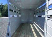 Interior of an empty white livestock trailer with wooden floor and open side rails under a bright blue sky.