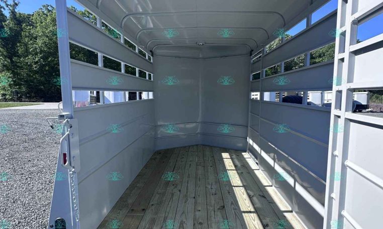Interior of an empty white livestock trailer with wooden floor and open side rails under a bright blue sky.