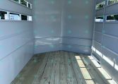 Empty light gray trailer interior with wooden deck and side rails, sunlit from outside.