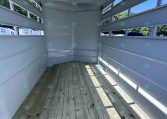 Interior of an empty white trailer with wooden floor and vented side walls, daylight entering from outside.