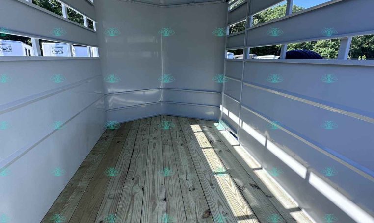 Interior of an empty white trailer with wooden floor and vented side walls, daylight entering from outside.