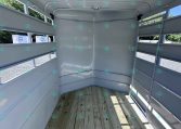 Interior of an empty white horse trailer with wooden floor and side slat windows, sun shining inside