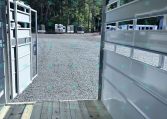 View from inside a white trailer looking out onto a gravel lot with several parked trailers and a wooded backdrop.