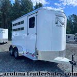 White aluminum horse trailer with dual axles in a gravel lot, trees in the background and other trailers nearby