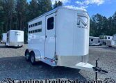 White aluminum horse trailer with dual axles in a gravel lot, trees in the background and other trailers nearby