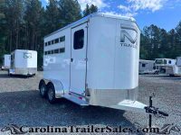 White aluminum horse trailer with dual axles in a gravel lot, trees in the background and other trailers nearby