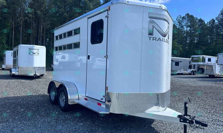 White aluminum horse trailer with dual axles in a gravel lot, trees in the background and other trailers nearby