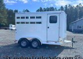 White horse trailer with a side door and sliding windows, parked on a gravel lot with trees in the background and a building nearby. Website watermark CarolinaTrailersales at the bottom.