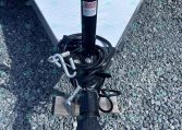 Close-up of a black trailer jack and safety chains attached to a trailer on a gravel surface, with a diamond-plate trailer wall in the background.