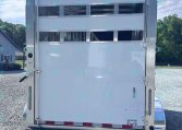 Rear of a white horse trailer with horizontal vent panels and metal latches, parked on a gravel lot.