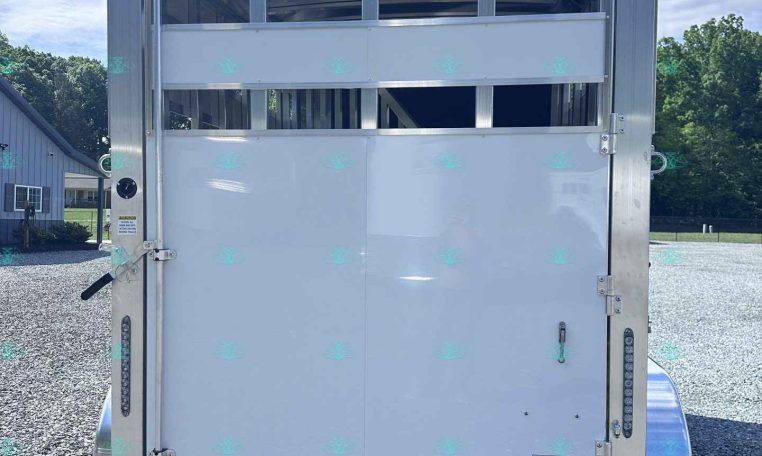 Rear of a white horse trailer with horizontal vent panels and metal latches, parked on a gravel lot.