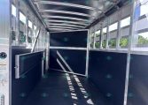 Interior of an empty aluminum trailer with open rear doors, black floor, and metal framing; blue sky visible outside.