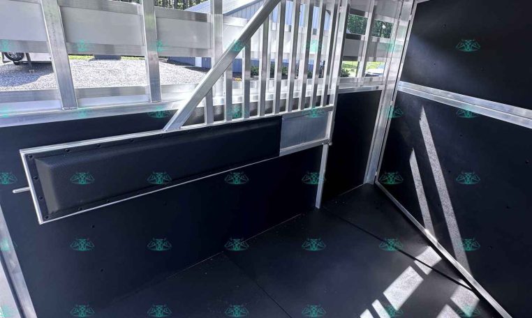 Interior of a silver aluminum trailer with exposed framing, black walls, and a metal stair/ramp leading to a higher deck; sunlit windows along one side.
