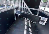Interior of a metal trailer showing a vertical-bar divider and slanted support beam, black wall panels, and rubberized floor. Light comes from side windows; watermark CarolinaTrailerSales.com visible at bottom.