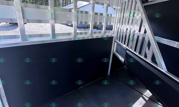Interior of a metallic trailer showing aluminum framing, a doorway with stairs, and a black interior wall on the right side. The area is well-lit with natural light outside.
