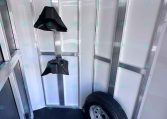 Interior of a metal trailer with a mounted spare tire and black wheel chocks hanging from the ceiling rails.