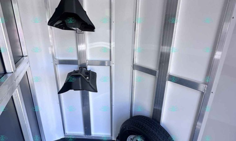 Interior of a metal trailer with a mounted spare tire and black wheel chocks hanging from the ceiling rails.