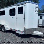 White tandem-axle horse trailer with two side windows on a gravel lot, front hitch visible under clear blue sky.