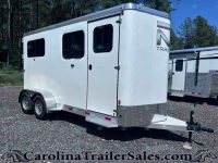 White tandem-axle horse trailer with two side windows on a gravel lot, front hitch visible under clear blue sky.