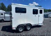 White horse trailer on a gravel lot with two axles and chrome wheels, windows along the side, and a second trailer visible in the background under a blue sky.