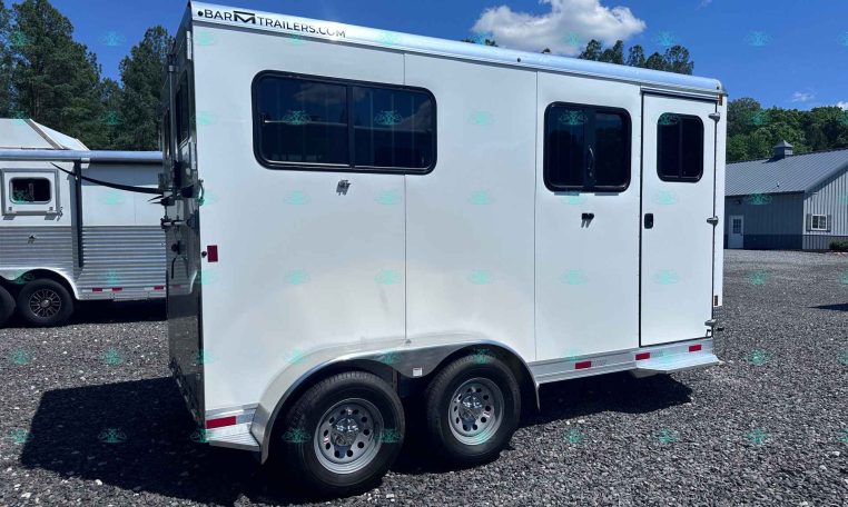 White horse trailer on a gravel lot with two axles and chrome wheels, windows along the side, and a second trailer visible in the background under a blue sky.