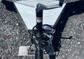 Close-up of a utility trailer hitch showing the jack, coupler, and safety chains on a diamond-plate trailer tongue, resting on gravel.