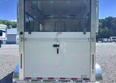 Rear view of a white horse trailer with stalls and interior partitions on a gravel lot under a blue sky