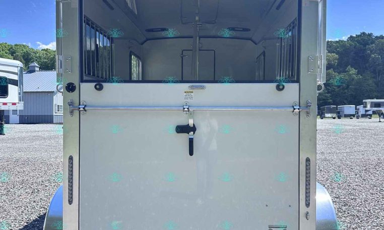 Rear view of a white horse trailer with stalls and interior partitions on a gravel lot under a blue sky