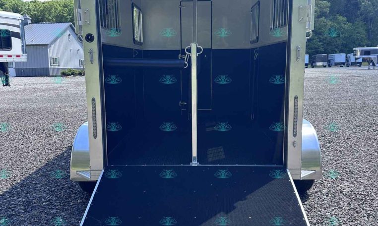 Open horse trailer with a lowered ramp, showing white and dark blue interior and a center divider in a gravel lot.