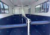 Interior of a blue and white horse trailer with divider and side stalls, padded rubber flooring, and barred windows on both sides