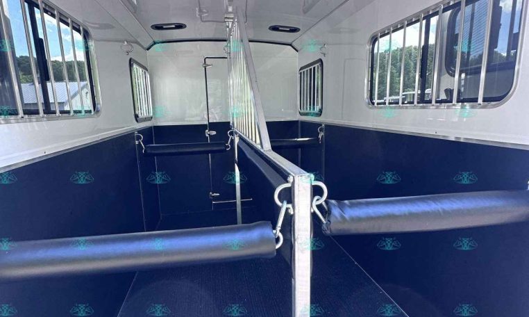 Interior of a blue and white horse trailer with divider and side stalls, padded rubber flooring, and barred windows on both sides
