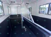 Inside a white horse trailer: black lower walls, a vertical divider gate, windows with bars, and a textured black rubber floor.