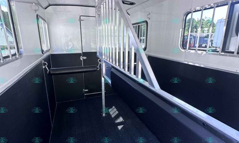 Inside a white horse trailer: black lower walls, a vertical divider gate, windows with bars, and a textured black rubber floor.