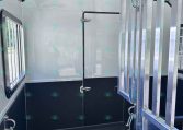 Interior of a horse trailer with white walls, a padded black bench, and metal divider rails along the doorway.