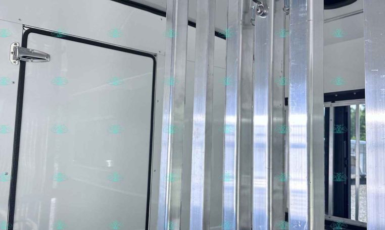 Interior view of a trailer with vertical aluminum support rails and a door latch in the frame divider area