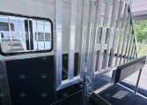 Interior of a metal trailer with vertical stalls and a lowered ramp, windowed side panel visible.